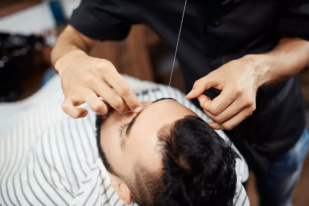 Mann, dem vom Friseur die Augenbrauen mit dem Faden gezupft werden